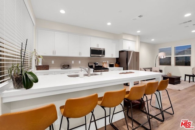 kitchen with backsplash, sink, light wood-type flooring, white cabinetry, and stainless steel appliances