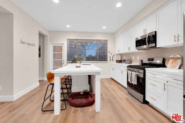 kitchen featuring white cabinets, a kitchen breakfast bar, light hardwood / wood-style flooring, an island with sink, and stainless steel appliances