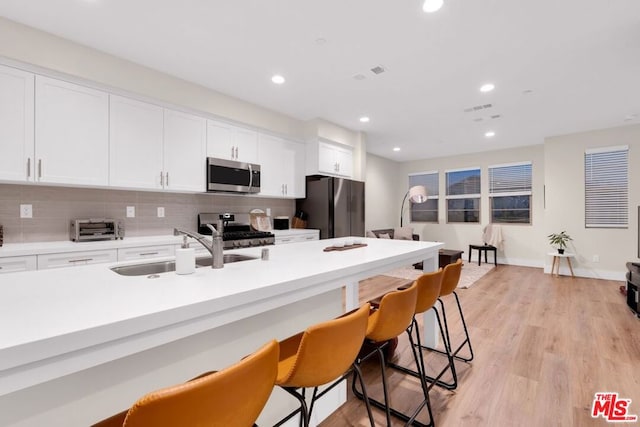 kitchen featuring backsplash, white cabinets, sink, light wood-type flooring, and appliances with stainless steel finishes