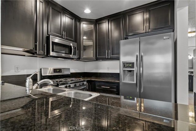 kitchen with dark brown cabinets, stainless steel appliances, dark stone counters, and sink