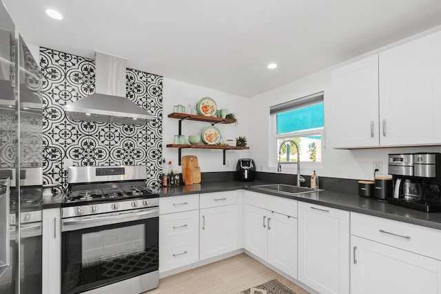 kitchen featuring white cabinetry, wall chimney range hood, gas range, and sink