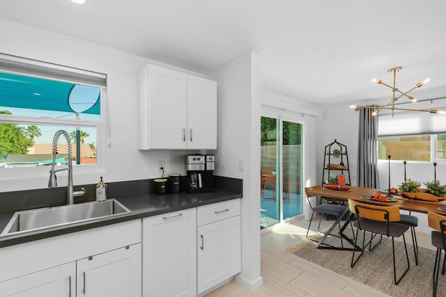 kitchen with an inviting chandelier, sink, pendant lighting, and white cabinets