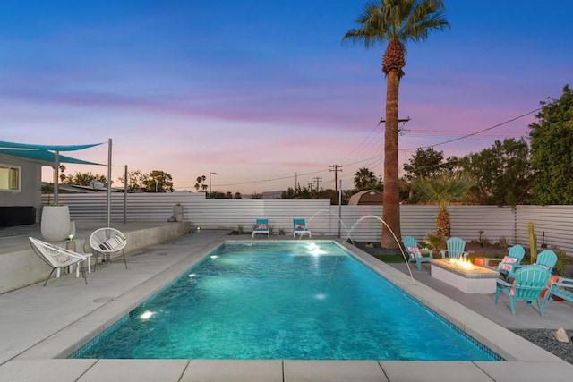 pool at dusk with a fire pit, a patio area, and pool water feature