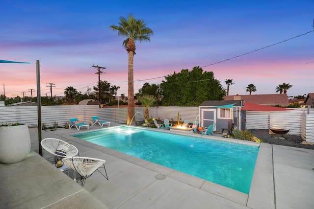 pool at dusk with a storage unit, an outdoor fire pit, and a patio