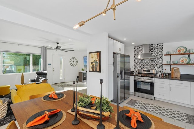 kitchen with ceiling fan, appliances with stainless steel finishes, backsplash, white cabinets, and wall chimney exhaust hood