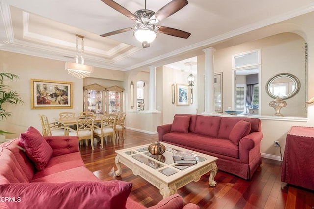 living room featuring ornate columns, dark hardwood / wood-style floors, ornamental molding, ceiling fan, and a tray ceiling