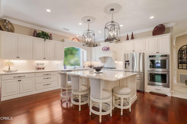 kitchen featuring a center island, white cabinetry, hanging light fixtures, ornamental molding, and stainless steel appliances