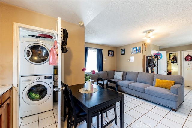 laundry area featuring stacked washer / drying machine, light tile patterned flooring, and a textured ceiling