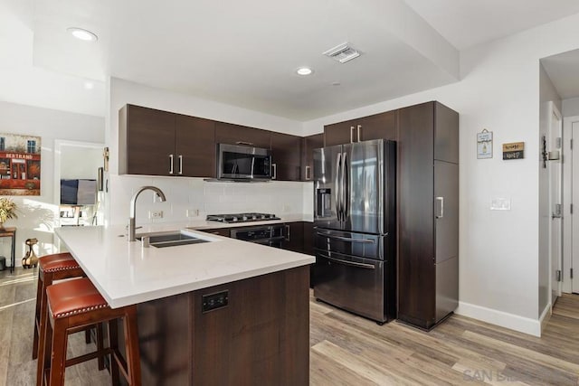 kitchen with kitchen peninsula, a breakfast bar area, appliances with stainless steel finishes, light hardwood / wood-style flooring, and sink