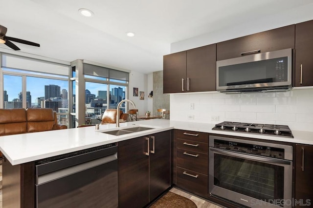 kitchen featuring kitchen peninsula, decorative backsplash, sink, dark brown cabinetry, and appliances with stainless steel finishes