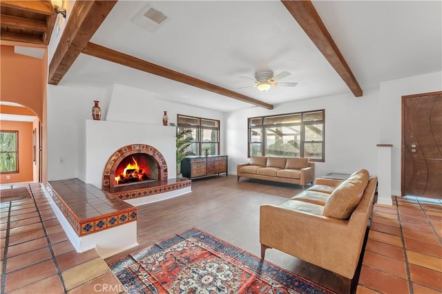 tiled living room featuring beam ceiling, a brick fireplace, and ceiling fan