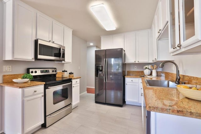 kitchen with stainless steel appliances, white cabinetry, light stone countertops, and sink