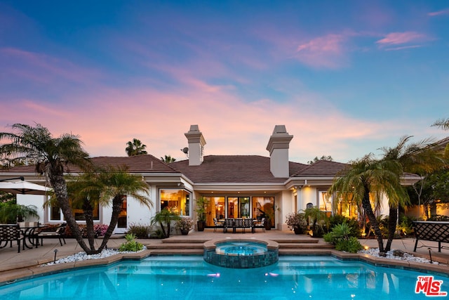 pool at dusk featuring an in ground hot tub and a patio area