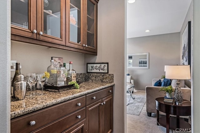 bar with dark brown cabinets, light stone counters, and light colored carpet