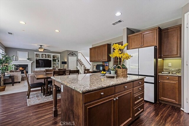 kitchen featuring a kitchen island, ceiling fan, light stone counters, white refrigerator, and dark hardwood / wood-style floors