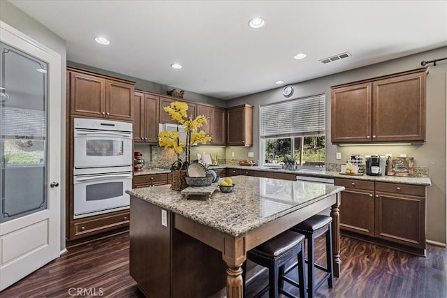 kitchen with dark hardwood / wood-style floors, double oven, light stone counters, and a kitchen island