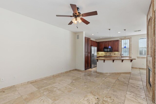 kitchen with stainless steel refrigerator with ice dispenser, a kitchen bar, tasteful backsplash, hanging light fixtures, and a center island with sink