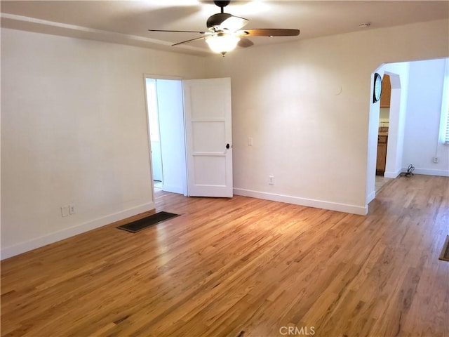 spare room with arched walkways, baseboards, ceiling fan, and light wood finished floors