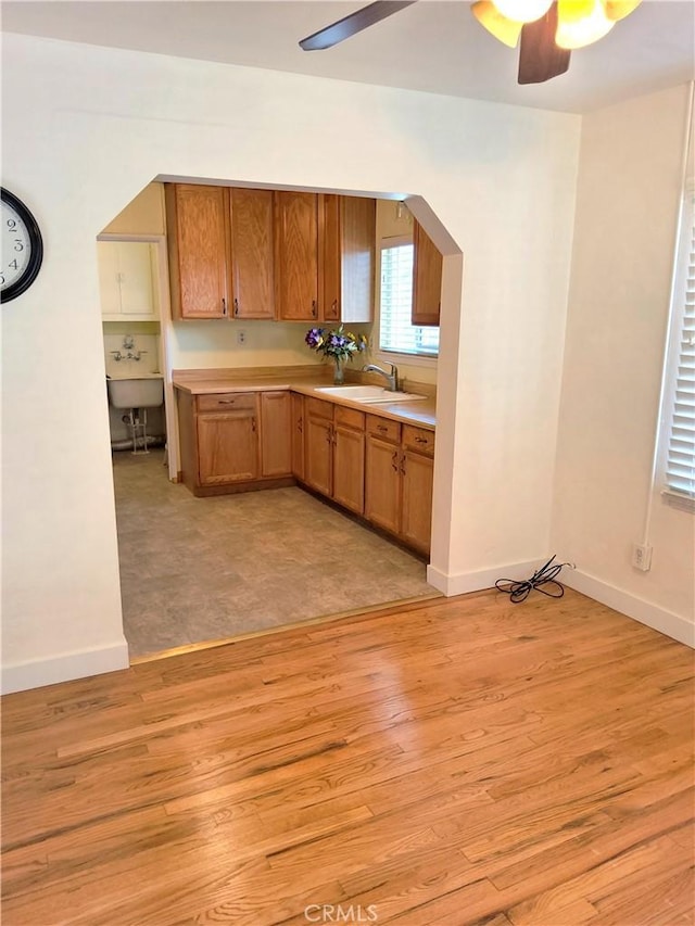 kitchen featuring arched walkways, brown cabinets, light countertops, light wood-style floors, and a sink