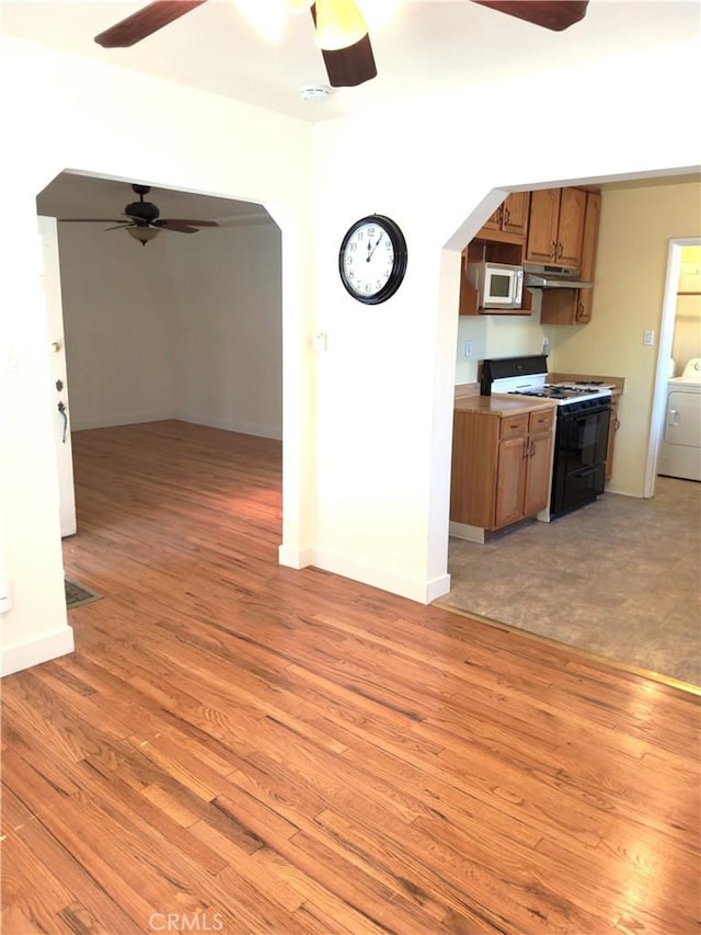 kitchen with arched walkways, light countertops, brown cabinets, stainless steel microwave, and range with gas cooktop