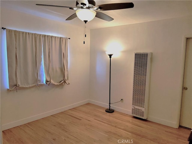 spare room featuring light wood-style floors, a heating unit, baseboards, and a ceiling fan