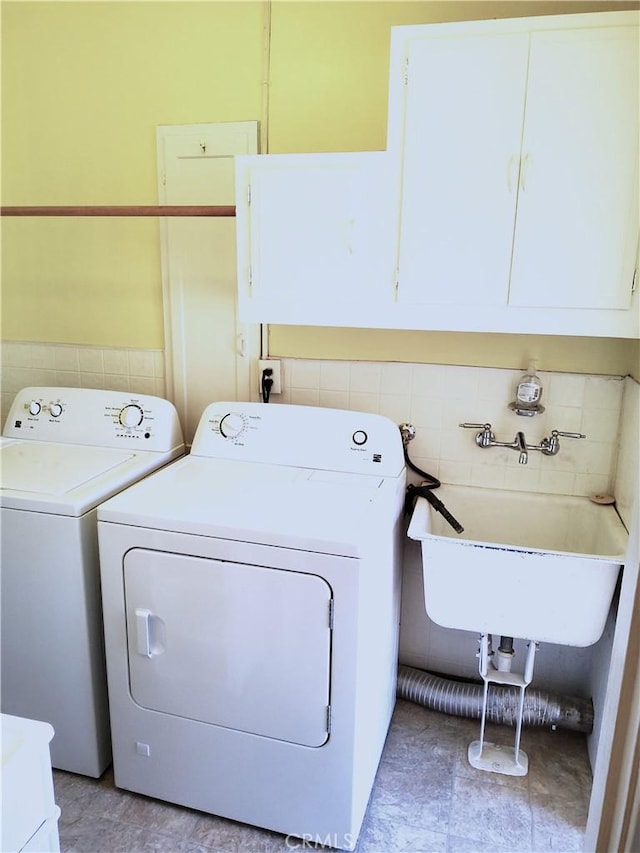 clothes washing area with washer / clothes dryer, a sink, cabinet space, and tile walls