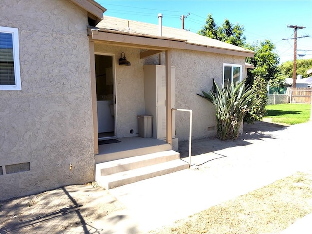 view of exterior entry with fence and stucco siding