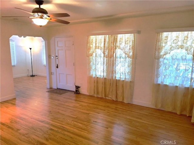 interior space with arched walkways, light wood-type flooring, a ceiling fan, and baseboards