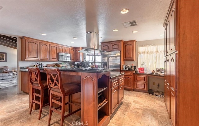 kitchen with island exhaust hood, a textured ceiling, stainless steel appliances, a kitchen island, and a breakfast bar area