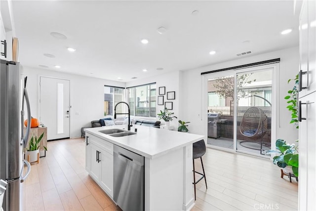 kitchen featuring a kitchen island with sink, sink, appliances with stainless steel finishes, a kitchen bar, and white cabinetry