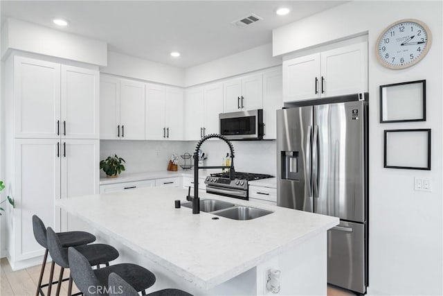 kitchen with a kitchen breakfast bar, light wood-type flooring, an island with sink, appliances with stainless steel finishes, and white cabinetry