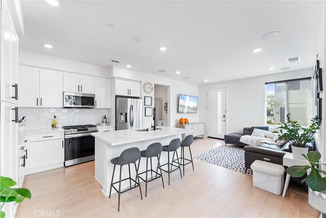 kitchen with a breakfast bar, white cabinets, light wood-type flooring, appliances with stainless steel finishes, and a kitchen island