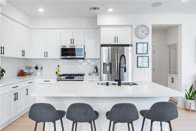 kitchen featuring light wood-type flooring, stainless steel appliances, sink, a center island with sink, and white cabinets