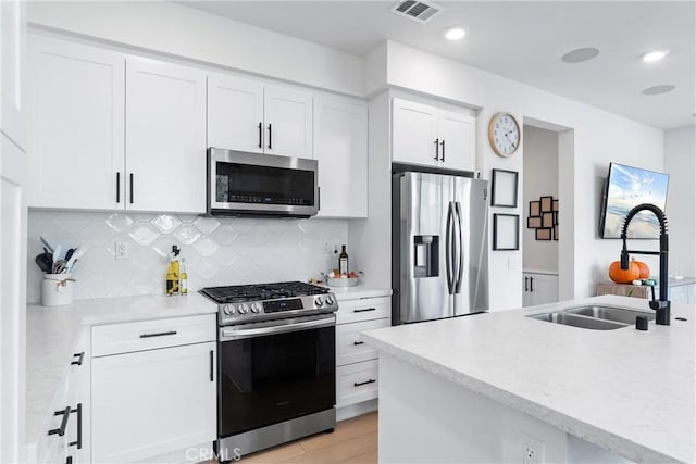 kitchen with white cabinetry, sink, light hardwood / wood-style flooring, backsplash, and appliances with stainless steel finishes