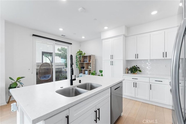 kitchen with white cabinetry, sink, stainless steel appliances, a kitchen island with sink, and light wood-type flooring