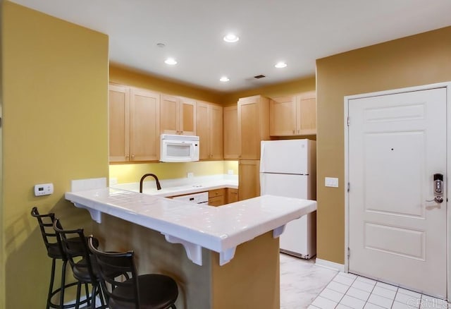 kitchen featuring white appliances, light brown cabinetry, a breakfast bar, and kitchen peninsula