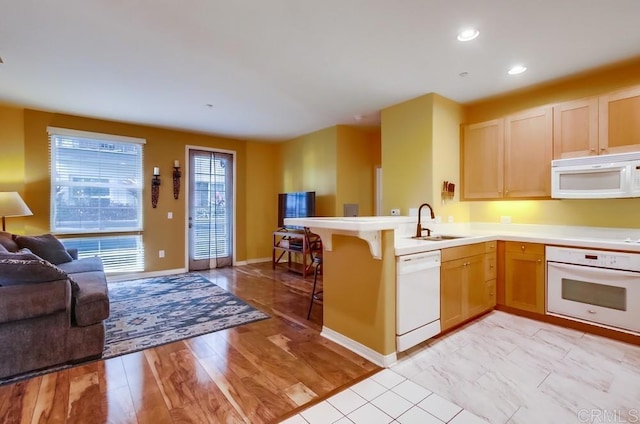 kitchen featuring kitchen peninsula, light brown cabinets, a kitchen breakfast bar, light wood-type flooring, and white appliances