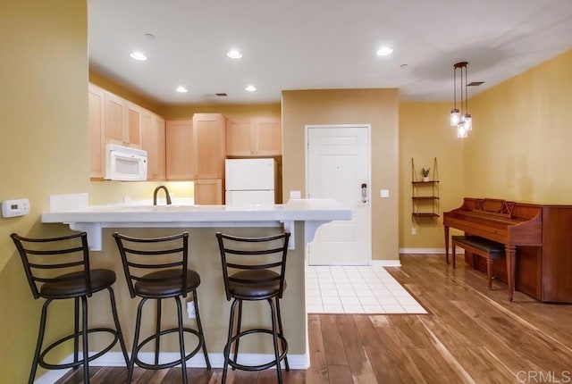 kitchen featuring kitchen peninsula, hardwood / wood-style floors, a kitchen breakfast bar, pendant lighting, and white appliances