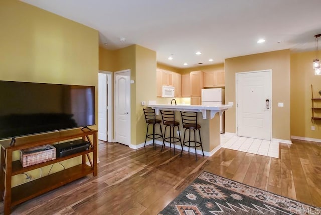 kitchen with a peninsula, a kitchen bar, light wood finished floors, and white appliances