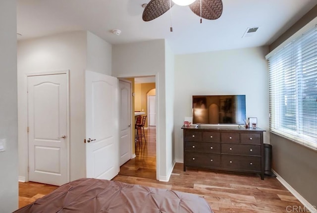 bedroom featuring a ceiling fan, light wood-type flooring, arched walkways, baseboards, and visible vents