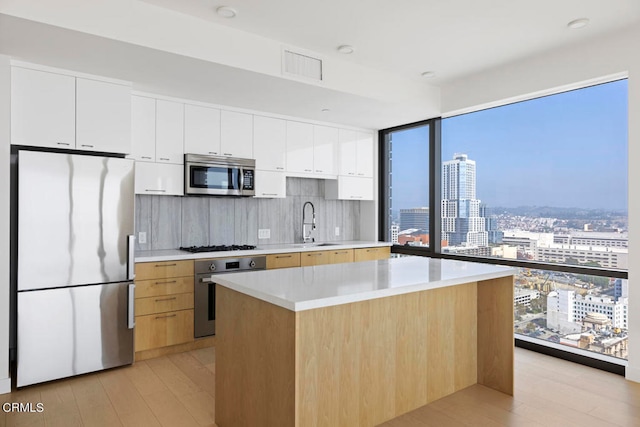 kitchen featuring tasteful backsplash, white cabinetry, stainless steel appliances, light hardwood / wood-style floors, and a center island