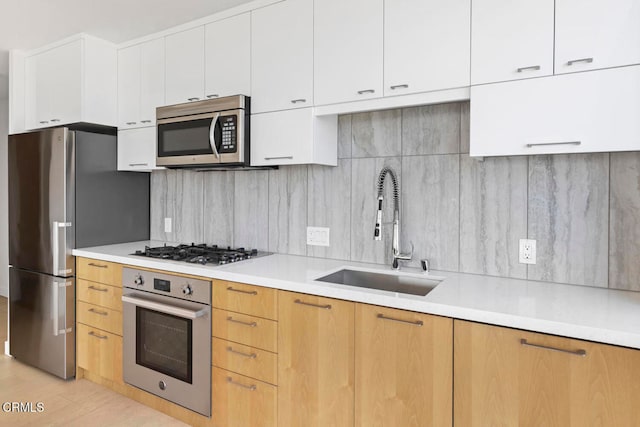 kitchen with appliances with stainless steel finishes, sink, backsplash, white cabinetry, and light hardwood / wood-style flooring