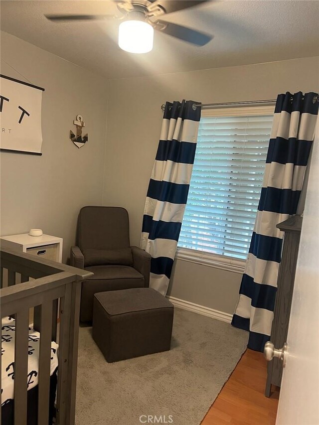 bedroom featuring ceiling fan, hardwood / wood-style flooring, and a nursery area