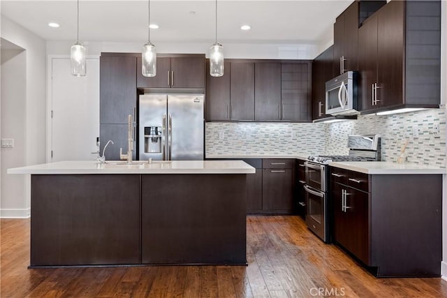 kitchen featuring dark brown cabinetry, hanging light fixtures, a center island with sink, and appliances with stainless steel finishes