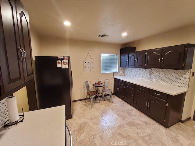 kitchen featuring backsplash, dark brown cabinetry, and black fridge