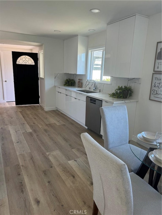 kitchen with tasteful backsplash, stainless steel dishwasher, sink, light hardwood / wood-style flooring, and white cabinets