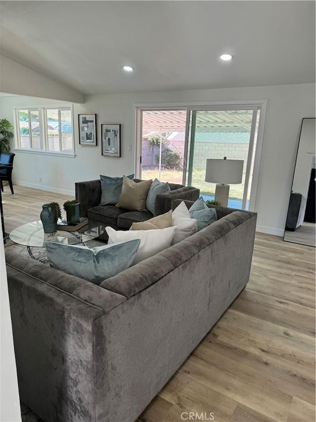 living room with light hardwood / wood-style flooring, a healthy amount of sunlight, and lofted ceiling