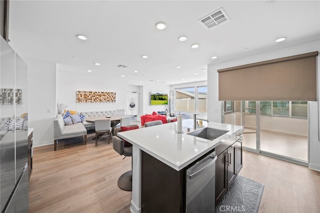 kitchen with stainless steel dishwasher, sink, light wood-type flooring, and a kitchen island with sink