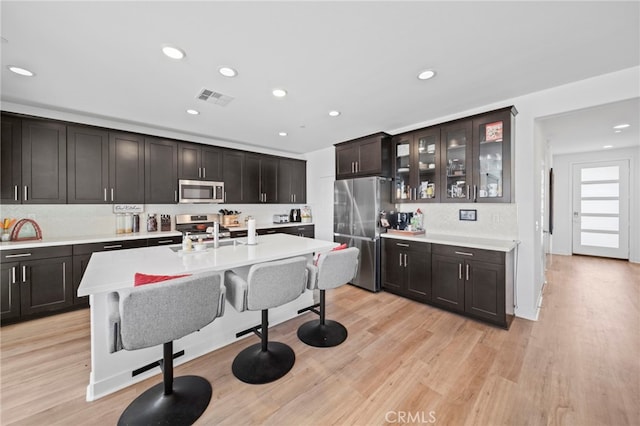 kitchen featuring light hardwood / wood-style flooring, appliances with stainless steel finishes, dark brown cabinetry, and a kitchen breakfast bar