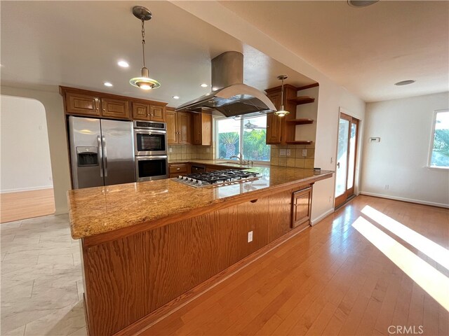 kitchen with island range hood, kitchen peninsula, stainless steel appliances, plenty of natural light, and light hardwood / wood-style floors